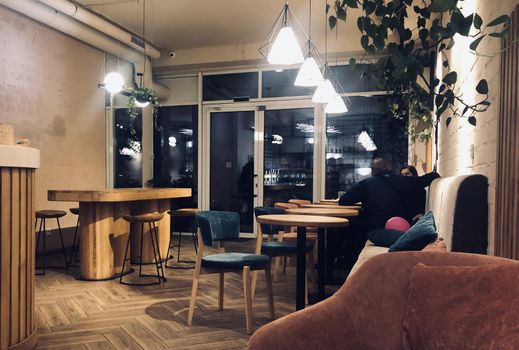 Inside the night cafe. Modern loft cafeteria with decorative parts in vintage style. Large dining table and wooden bar chairs with steel legs. Comfortable romantic place for date like restaurant.