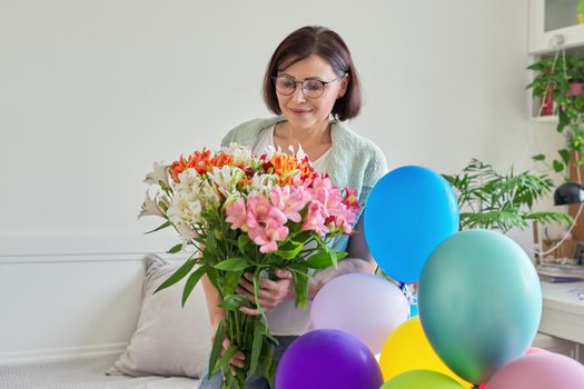 Birthday, 45 years old, happy middle-aged female with bouquet of flowers and balloons at home in the room. Mature age, celebration, anniversary, people concept