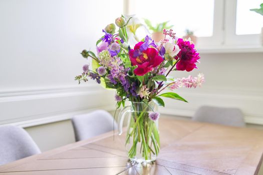 Bouquet of bright flowers on the table in jug. Flowers and buds of peonies irises lupine, season spring summer, home natural decor, holiday, gift concept