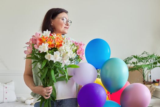 Birthday, 45 years old, happy middle-aged female with bouquet of flowers and balloons at home in the room. Mature age, celebration, anniversary, people concept