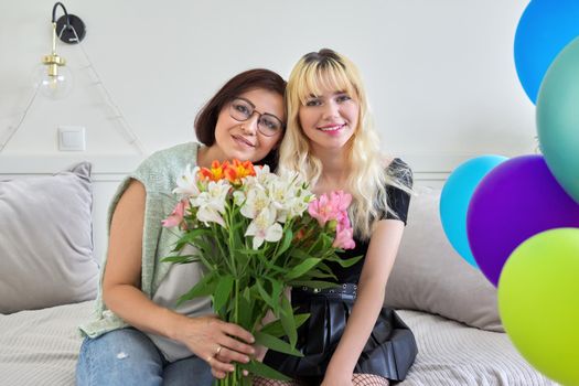 Portrait of happy smiling mom and teenage daughter, birthday celebration, women with bouquet of flowers colored balloons. Holiday, birthday, parent teenager relationship concept