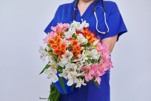 Health day, close-up bouquet of flowers in the hands of doctor nurse. Female medic in blue medical uniform, protective gloves with stethoscope on light background