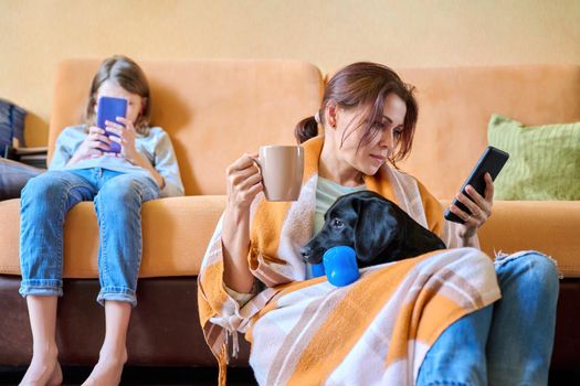 Family, home, lifestyle, pets, technology, communication, relaxation, e-learning, online reading, leisure. Mom, daughter child and dog sitting at home on couch looking at smartphone screen
