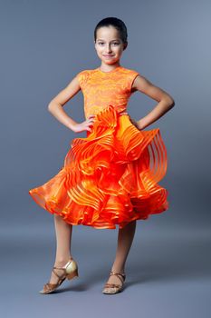 Kids sport dancing, kid girl in orange sport dress posing in dance pose looking at camera on gray studio background.