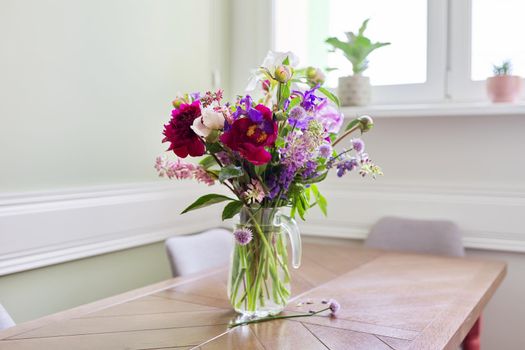 Bouquet of bright flowers on the table in jug. Flowers and buds of peonies irises lupine, season spring summer, home natural decor, holiday, gift concept