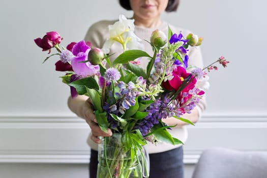 Bouquet of bright flowers of peonies irises lupins in the hands of woman close-up, female at home