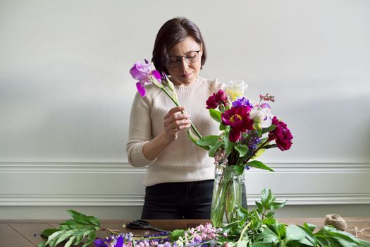 Mature woman at home with spring flowers. Female making bouquet, placing flowers in jug of water. Spring summer season, floristry, home decoration, natural beauty concept