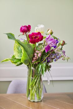 Bouquet of bright flowers on the table in jug. Flowers and buds of peonies irises lupine, season spring summer, home natural decor, holiday, gift concept