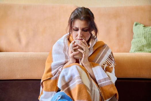 Winter, autumn, cold season. Middle-aged woman under a warm woolen blanket with cup of hot drink