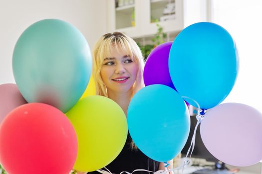 Close up of colored balloons and happy smiling face of blonde teen female. Birthday 16, 17 years, holiday, happiness, joy, bright balloons background