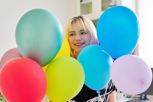 Close up of colored balloons and happy smiling face of blonde teen female. Birthday 16, 17 years, holiday, happiness, joy, bright balloons background