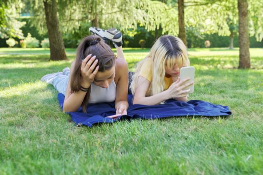 Two young female teenagers lying on grass in park with smartphones. Girls looking at phone screen. Youth, adolescents, technology, lifestyle, leisure concept