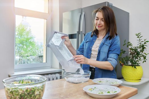 Woman taking ice cubes into bowl in kitchen, modern refrigeration equipment, home chrome refrigerator background