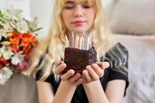 Birthday of female teenager, girl with birthday small cake with extinguished candles, bouquet of flowers background. Holiday, teens, age, celebration concept