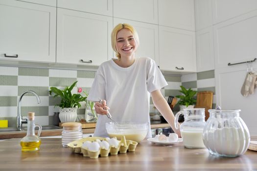 Female teenager preparing food at home, girl in the kitchen, ingredients for making pancakes eggs flour milk sugar on the table. Eating at home, healthy homemade food, teen hobbies