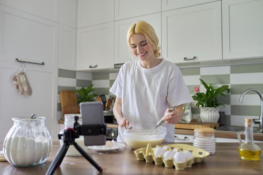 Female teenager learns to cook pancakes, watching video recipe on smartphone, in home kitchen. Cooking home food, culinary hobby, learning cooking class, teenagers, people concept