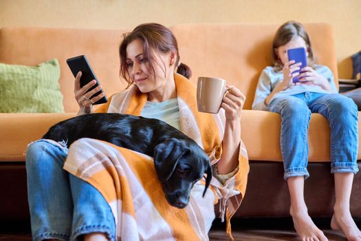 Family, home, lifestyle, pets, technology, communication, relaxation, e-learning, online reading, leisure. Mom, daughter child and dog sitting at home on couch looking at smartphone screen