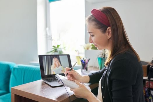 Woman teacher teaching at home online, distance learning. Female sitting at home at table with laptop on virtual meeting with teenage student, video call. E-learning modern technologies in education