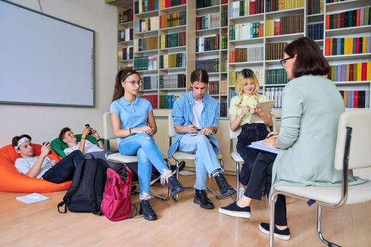 Female mentor teacher working with male teenage high school students in the library. Education, knowledge, adolescence, consultation, support, school, college concept