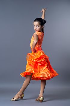 Kids sport dancing, kid girl in orange sport dress posing in dance pose looking at camera on gray studio background.