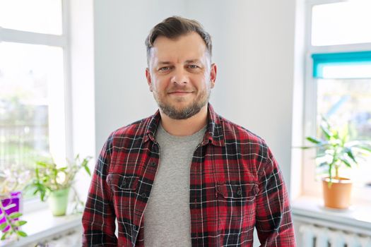 Portrait of 40 years old man, smiling male in plaid casual shirt looking at camera, home living room interior background