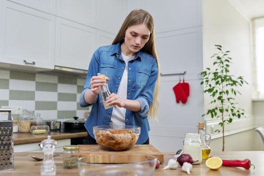 Young woman cooking chicken for holiday, marinating with spices with black pepper salt, at home in kitchen. Culinary blog, recipe, hobby and leisure.