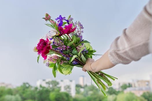 Close-up of bright bouquet of flowers in female hand. Fresh flowers and buds of peonies iris lupine in flower arrangement. Season spring summer, natural beauty, background open window blue sky