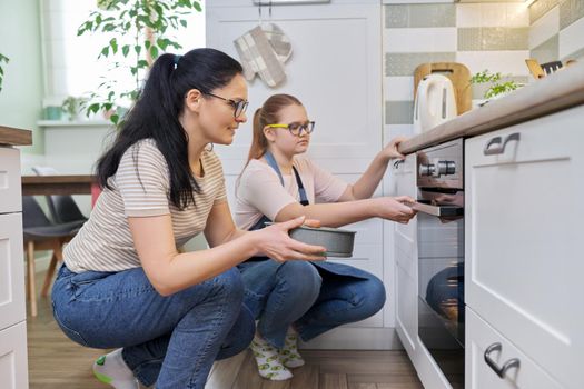 Mother and daughter preparing cake together, putting mold with dough in oven. Family, lifestyle, eating at home concept