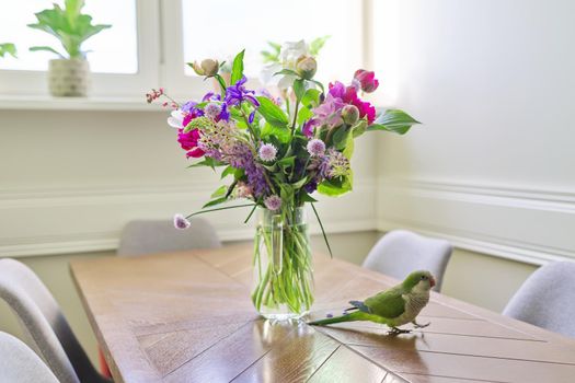 Parrot green quaker pet and bouquet of flowers on the table. Bright beautiful colors of nature, natural beauty, home, pets, flower decoration