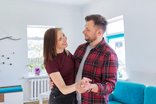 Happy romantic middle aged couple in love dancing, husband and wife dancing at home in living room, in home casual clothes. Relationships, lifestyle, communication, home life, middle-aged people