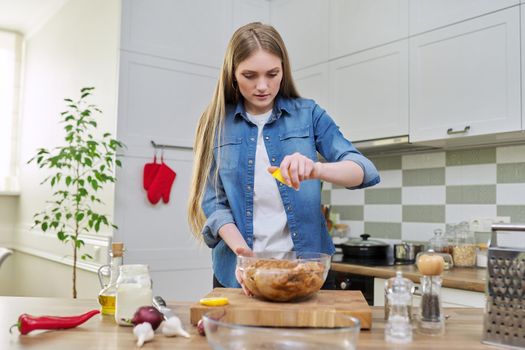 Young woman cooking chicken for the holiday, marinating with spices with black pepper, salt and lemon, at home in kitchen. Culinary blog, recipe, hobby and leisure.