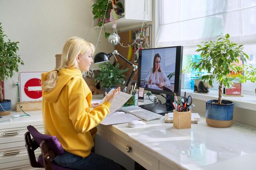 Teenager girl sitting at home studying online using home computer. Education and distance learning, video broadcast of lesson. Homeschooling, elearning, modern technologies in education