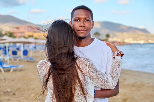 Happy young couple hugging, man's face close up. Interracial couple, african american man looking at camera on summer beach, relationship, love, happiness, people, family, tourism, travel