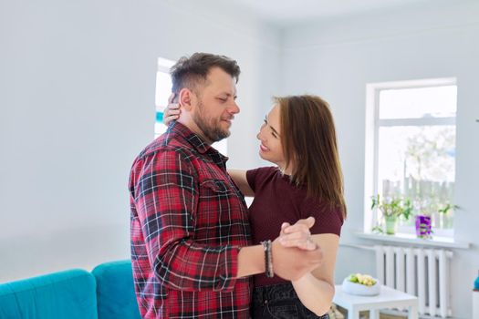 Happy romantic middle aged couple in love dancing, husband and wife dancing at home in living room, in home casual clothes. Relationships, lifestyle, communication, home life, middle-aged people