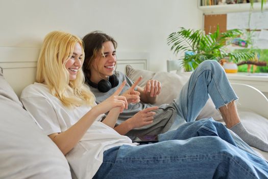 Happy laughing hipster teenagers male and female having fun using smartphone together. Couple using video call, watch funny photos videos. Lifestyle, technology, friendship, communication, adolescents