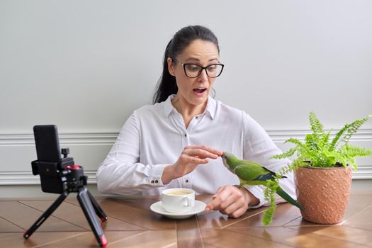 Woman playing with her pet parrot at home, bird biting woman's finger.