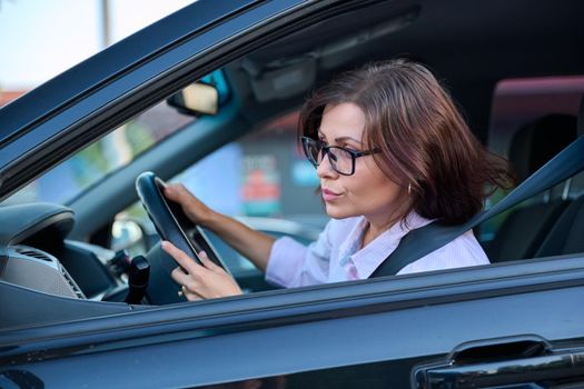 Middle-aged woman driver driving a car. Beautiful adult female with glasses, lifestyle, people, transport concept