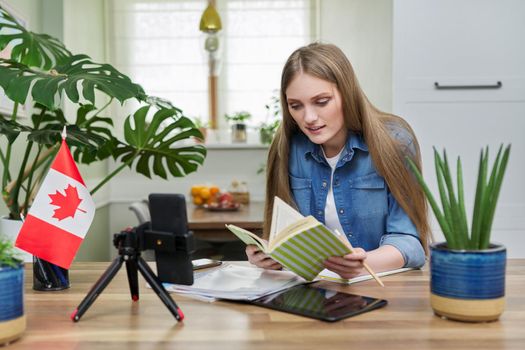 Online learning, distance lessons, e-learning, teenage female university student sitting at home looking at smartphone screen, video meeting, on table canadian flag. Canada, education, study concept