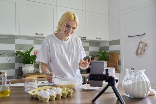 Female teenager learns to cook pancakes, watching video recipe on smartphone, in home kitchen. Cooking home food, culinary hobby, learning cooking class, teenagers, people concept