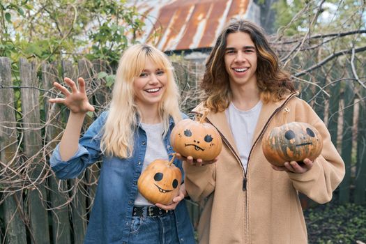 Couple of laughing teenagers with pumpkins having fun outdoors in the garden, halloween autumn holiday, youth concept