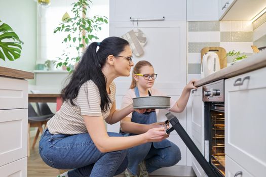 Mother and daughter preparing cake together, putting mold with dough in oven. Family, lifestyle, eating at home concept