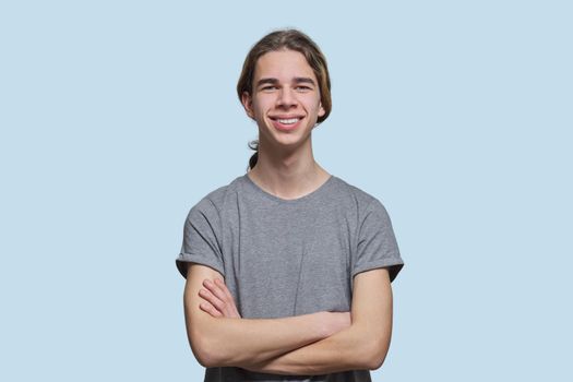 Portrait of happy smiling guy 15, 16 years old teenager with crossed arms, handsome trendy male looking at the camera on light studio background