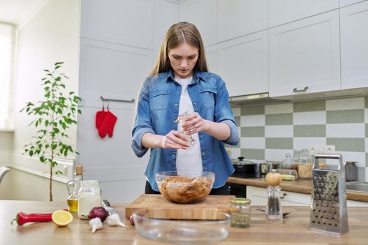 Young woman cooking chicken for holiday, marinating with spices with black pepper salt, at home in kitchen. Culinary blog, recipe, hobby and leisure.