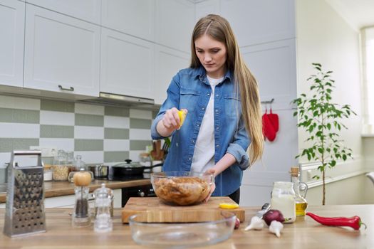 Young woman cooking chicken for the holiday, marinating with spices with black pepper, salt and lemon, at home in kitchen. Culinary blog, recipe, hobby and leisure.