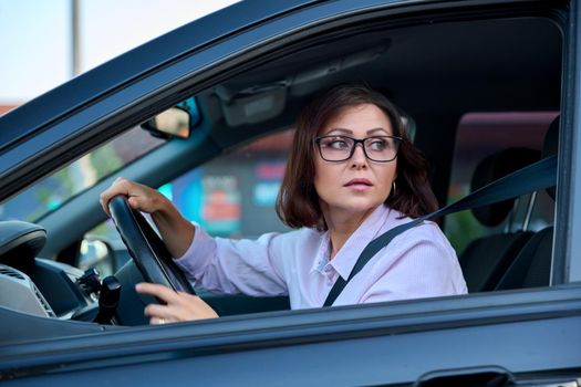 Middle-aged woman driver driving a car. Beautiful adult female with glasses, lifestyle, people, transport concept