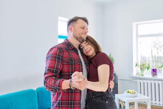 Happy romantic middle aged couple in love dancing, husband and wife dancing at home in living room, in home casual clothes. Relationships, lifestyle, communication, home life, middle-aged people