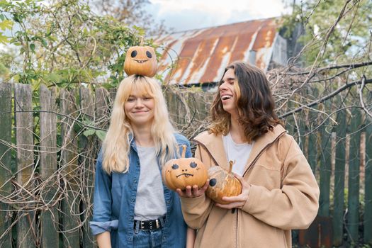 Couple of laughing teenagers with pumpkins having fun outdoors in the garden, halloween autumn holiday, youth concept