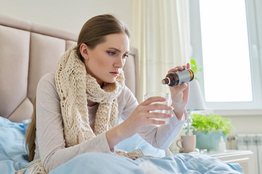 Sick woman at home in bed adding drops of medicine to a glass of water. Medicine, pharmacology, flu season, seasonal diseases, people concept