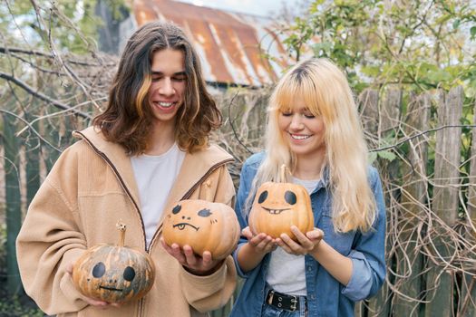 Couple of laughing teenagers with pumpkins having fun outdoors in the garden, halloween autumn holiday, youth concept