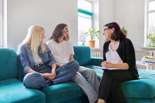 Professional female social worker, teacher, counselor, psychologist talking with teenagers, discussing school projects, organizing activities. Smiling, positive college and high school students